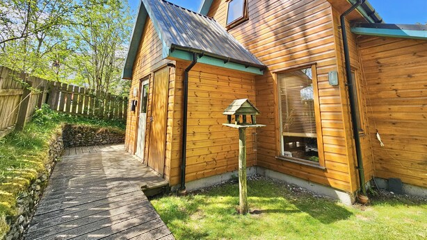A wooden cabin with a metal roof, a wooden deck, and a stone wall.