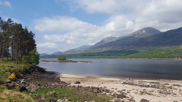 A natural landscape with a lake, mountains, and a rocky shoreline.