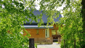 A wooden cabin with a gravel path leading to it, surrounded by trees and a stone wall.