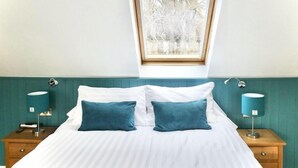A bedroom with a skylight, a bed with white bedding and two teal pillows, and two bedside tables with lamps.