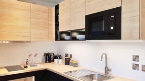 A modern kitchen with black and light wood cabinetry, a stainless steel sink, and a built-in microwave.