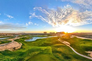 Vista aérea de um campo de golfe, com um rio, caminhos e edifícios ao longe.