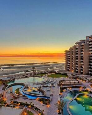 Ein Resort mit mehreren Schwimmbecken, einem großen Gebäude und Blick auf den Sonnenuntergang.