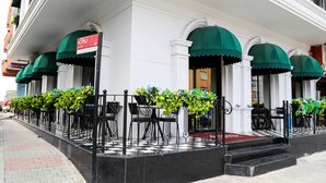 A hotel with a checkered floor, outdoor seating with green awnings, and a 'For Sale' sign. - Axu Airport Hotel (Arnavutköy)