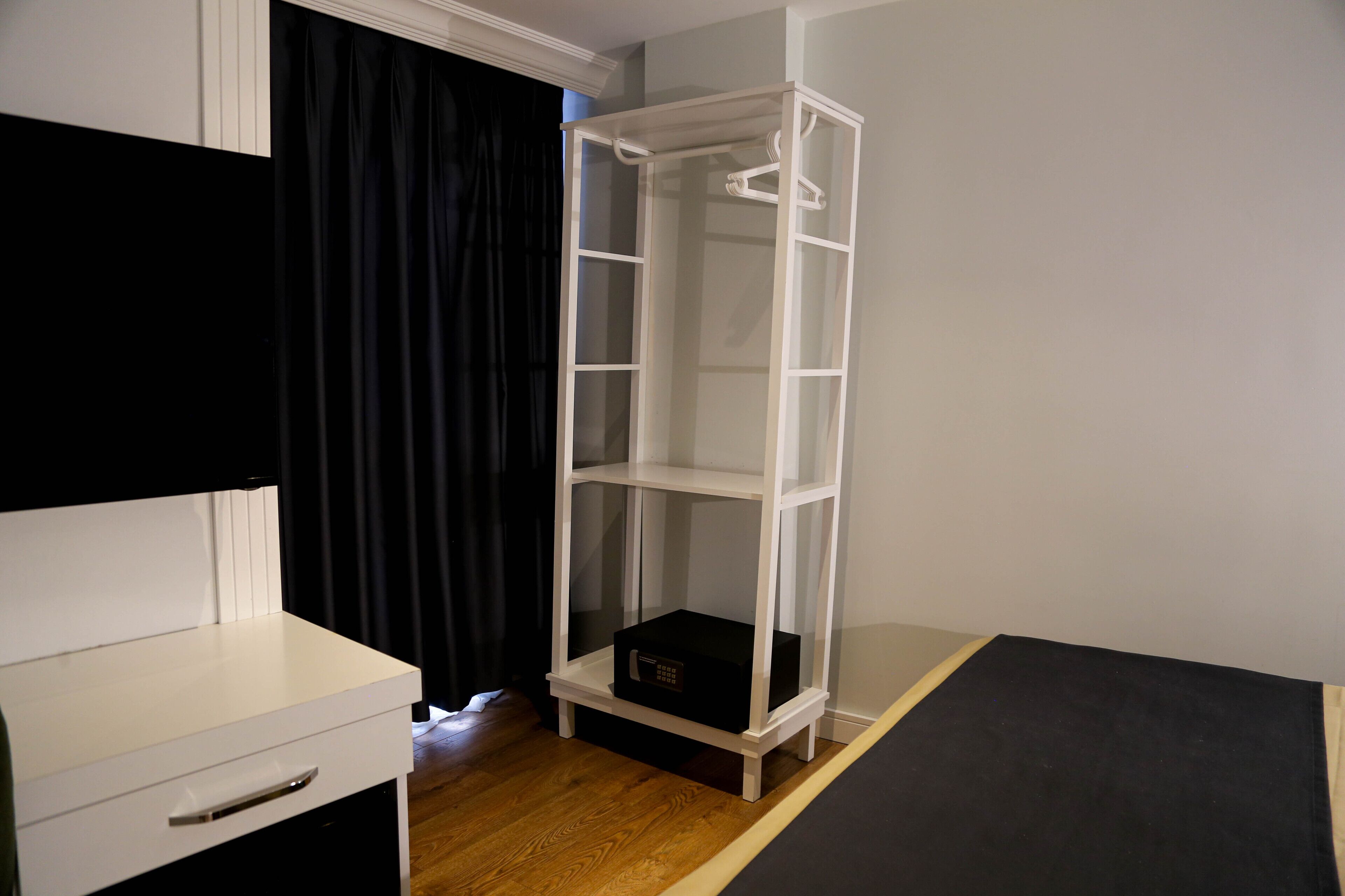 A room with a white desk, a black curtain, a white shelving unit, and a black mattress.
