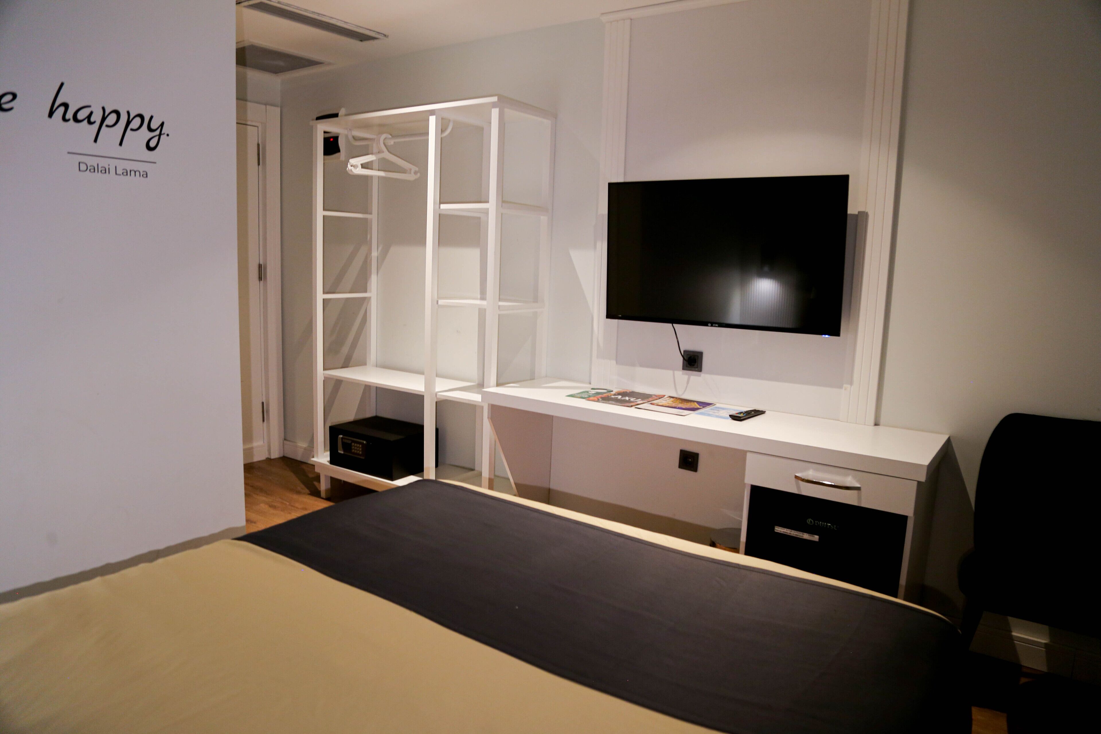 A modern bedroom with a bed, a desk with a TV, a wardrobe, and a wall with a motivational quote.