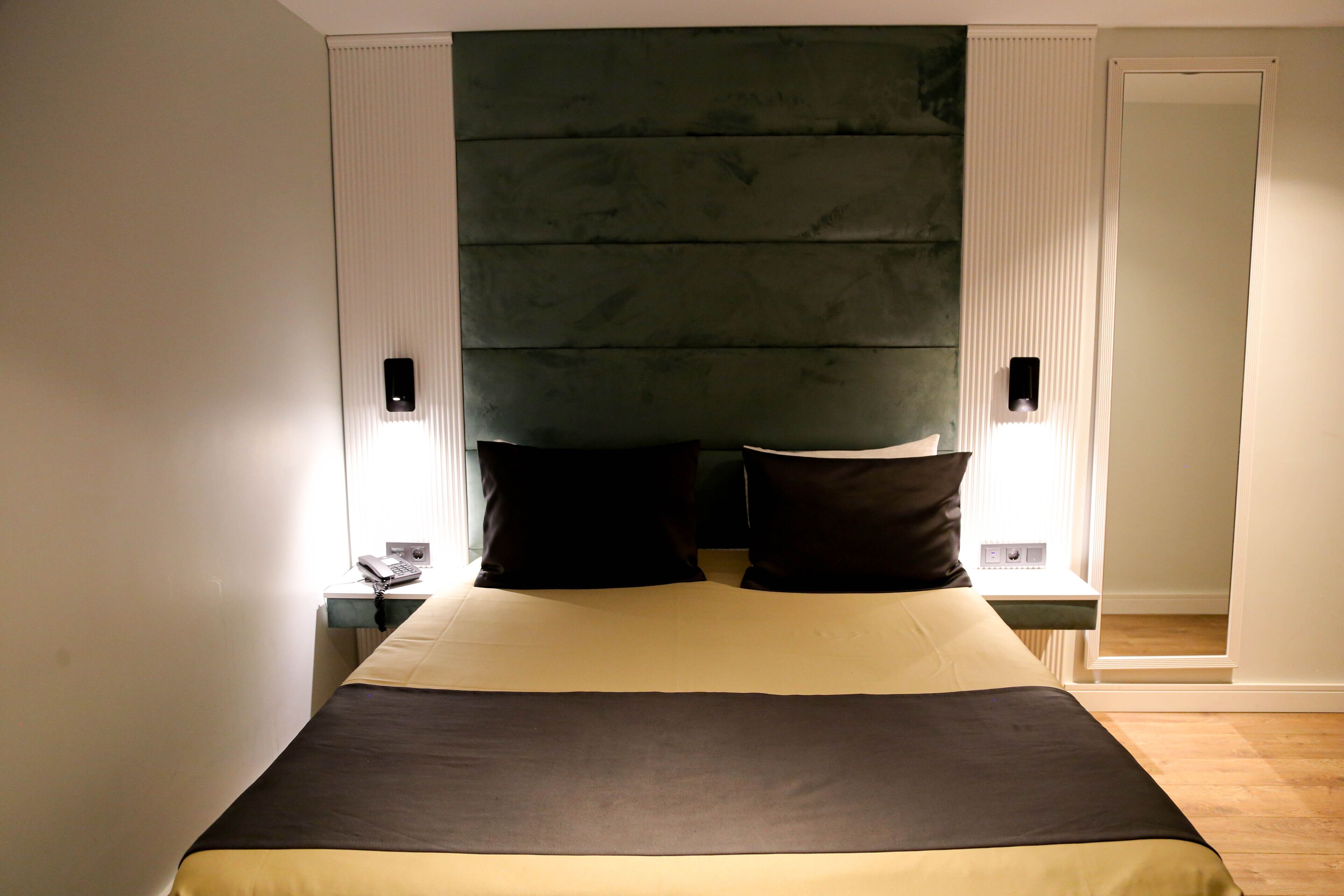 A neatly made bed with a dark headboard, two bedside lamps, and a nightstand with a phone.