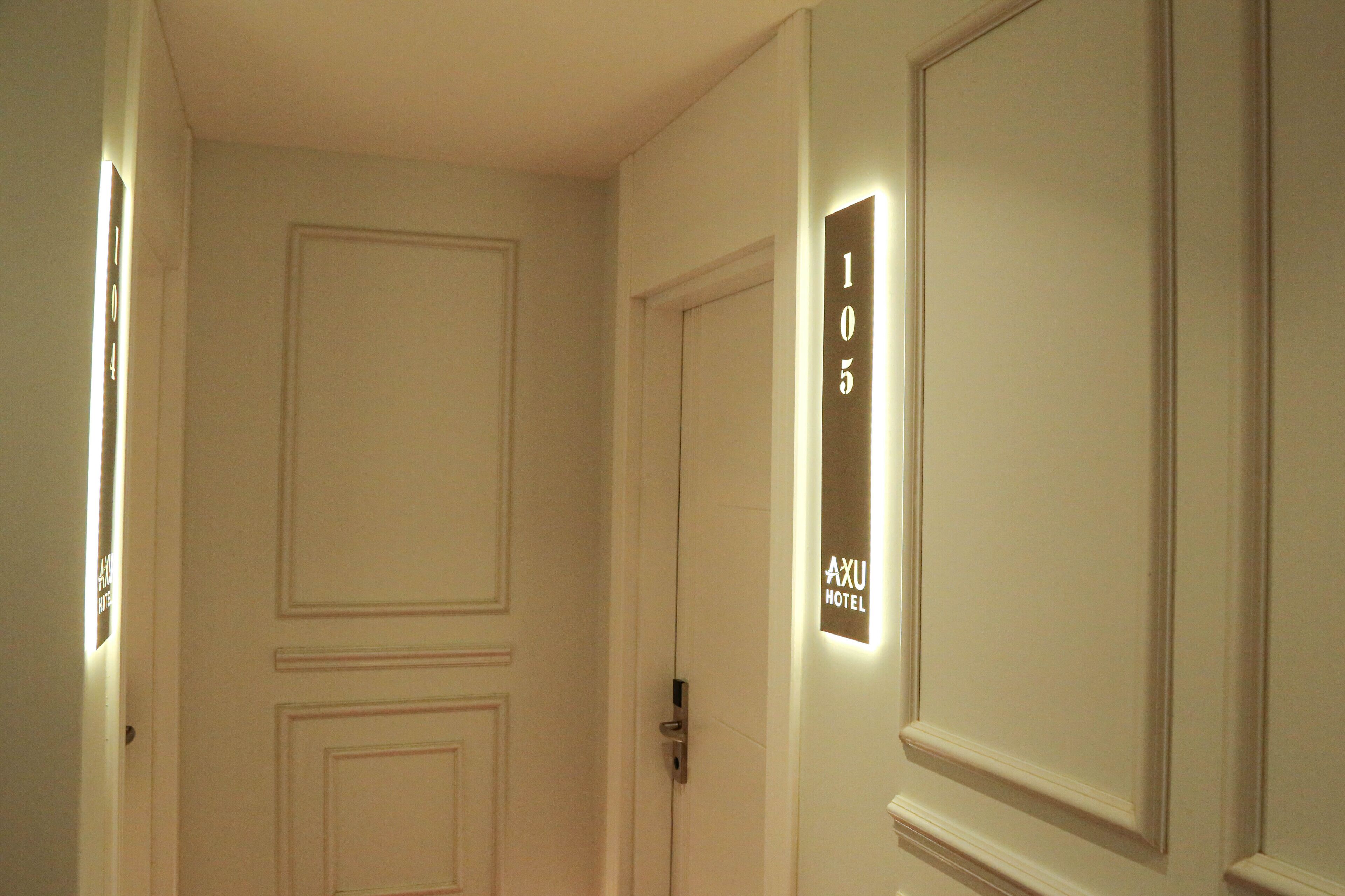 Entrada a una habitación de hotel con una puerta marcada con el número "105" y un letrero que indica "AXU HOTEL".