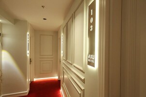 Un pasillo con alfombra roja, una puerta y una pared con un letrero que dice 'AXU HOTEL'.