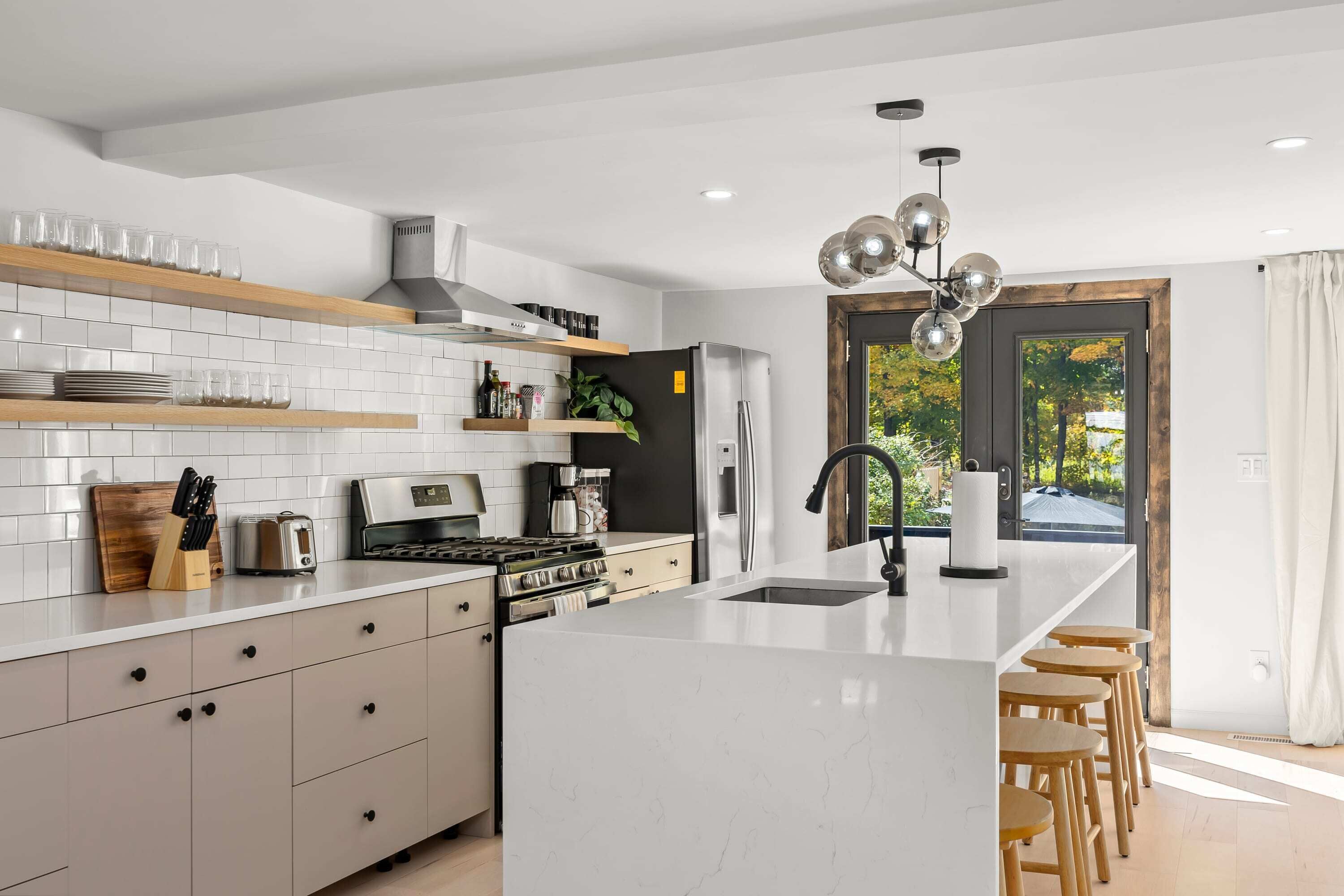 Una cucina moderna con mobili bianchi, un'isola centrale, sgabelli di legno e un'ampia finestra.