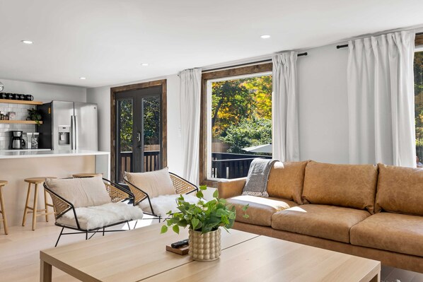 Un salon moderne comprenant un canapé, des fauteuils, une table basse et un coin cuisine.