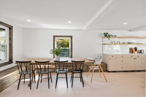 Une cuisine moderne avec une table et des chaises en bois, un plan de travail blanc carrelé et une fenêtre donnant sur un paysage verdoyant.