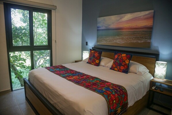 Un dormitorio con una cama grande, vistas al exterior a través de una ventana y un cuadro de un atardecer en la pared.