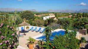 A pool area with lounge chairs, a thatched umbrella, and a view of mountains.