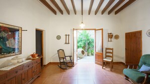 A spacious room with a tiled floor, wooden furniture, a painting, and a view of a garden through an open door.