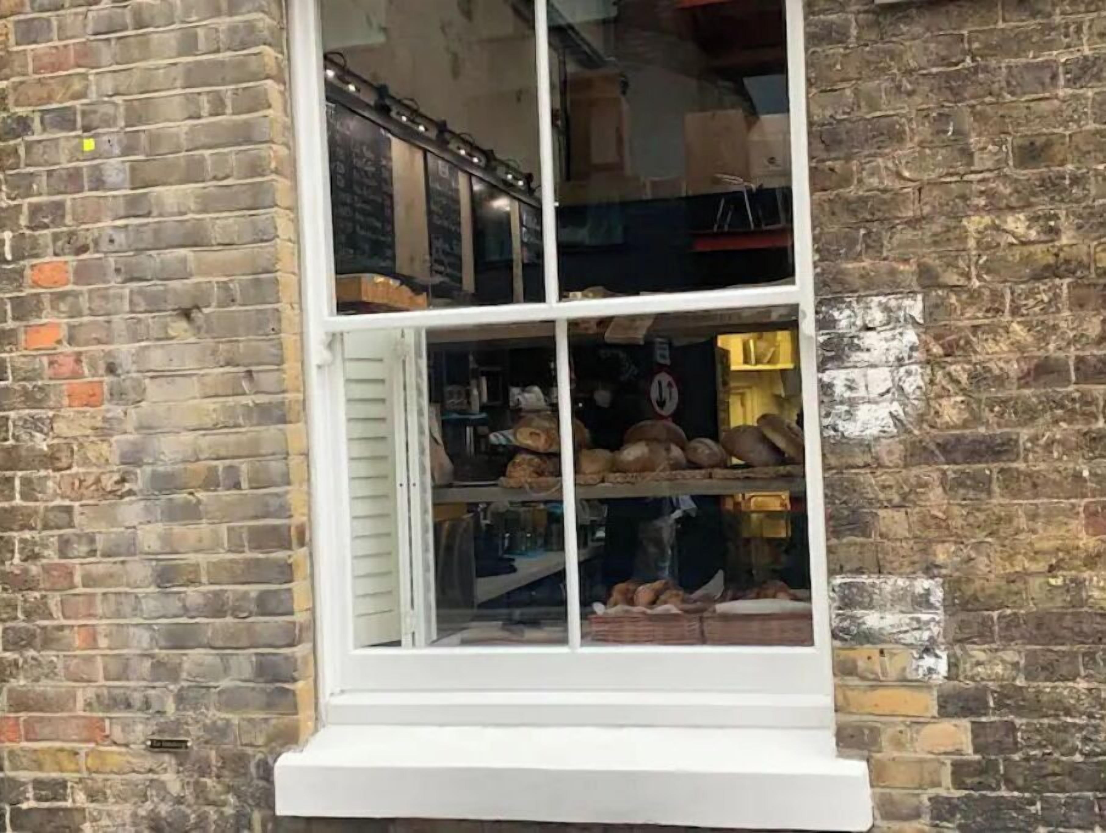 Ein Fenster mit weißem Rahmen, eine Ziegelwand und ein Regal mit Brot darin.
