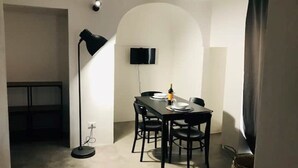 A compact dining area with a table set for two, a black floor lamp, and a flat-screen TV mounted on the wall. - The cave of benikulà ancient Pantelleria Dammuso Andrea 2 (Scauri)