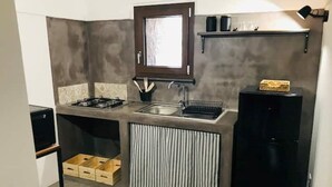 A compact kitchen with a gas stove, sink, and a black refrigerator. - The cave of benikulà ancient Pantelleria Dammuso Andrea 2 (Scauri)