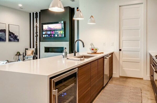A modern kitchen with a large island, built-in oven, and a flat-screen TV mounted above the island.