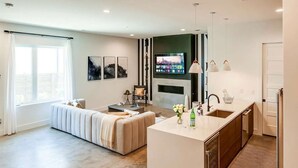 A modern living room with a sofa, a TV mounted on the wall, and a kitchen area with a sink and countertop. - Nashville music-themed house sleeps 10 near Belmont Mansion (Nashville)