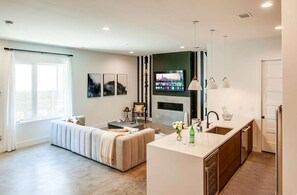 Ein modernes Wohnzimmer mit einer Couch, einem an der Wand befestigten Fernseher und einer Küchenzeile mit Spüle und Arbeitsplatte.