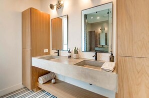 A modern bathroom with a double sink vanity, wooden cabinetry, a large mirror, and a glass shower enclosure. - Summer rooftop deck, gourmet kitchen, cornhole games near Broadway (Nashville)