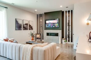 Ein modernes Wohnzimmer mit Flachbildfernseher über einem Kamin, einer Couch und einem Couchtisch.