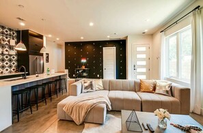 A modern living room with a sofa, a coffee table, and a kitchen area with a refrigerator and bar stools.