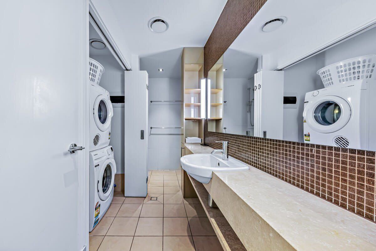 Une salle de bain moderne équipée de deux machines à laver, d’un lavabo et d’un miroir.