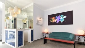 Ein Empfangsbereich mit einer Bank, einem Wandbild und einem Schreibtisch mit Computer.