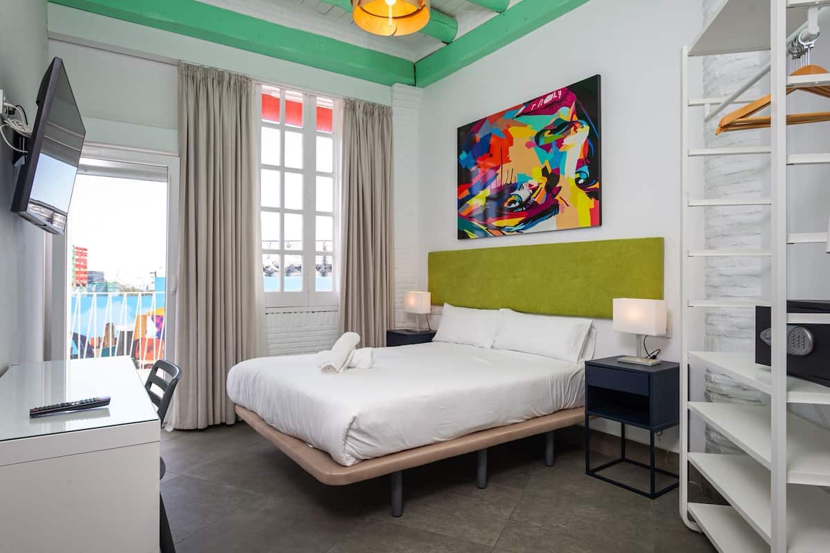 Une chambre d’hôtel avec un lit, des tables de chevet, une télévision, une fenêtre avec des rideaux, une peinture abstraite aux couleurs vives et une vue sur l’extérieur.