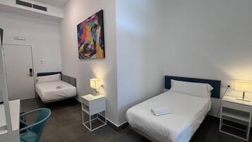 Habitació d'hotel amb dos llits individuals, una taula de treball, una cadira, un quadre a la paret i una porta.