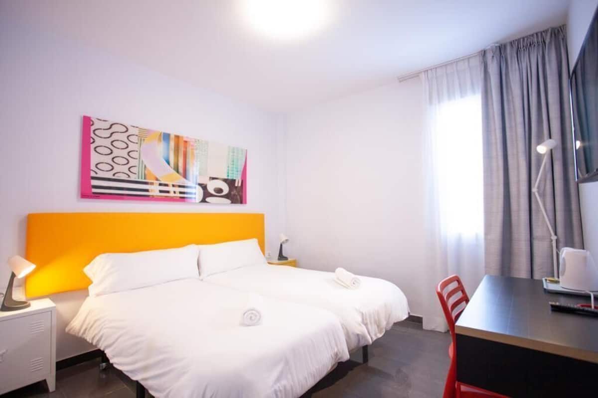 Une chambre d’hôtel avec un lit, un bureau, une chaise, une lampe et un tableau au mur.