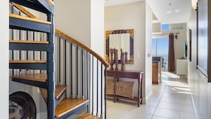A modern interior with a wooden staircase, a dining area with a mirror, and a view to the outside. - Ariel Dunes II Penthouse 2403 - Top-Floor, Terrace Balcony, Stunning Gulf Views! (Miramar Beach)