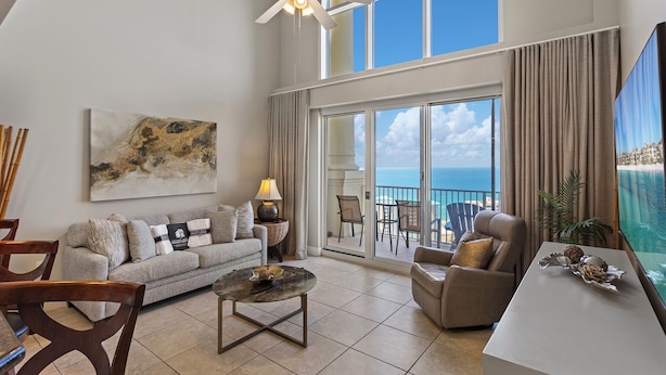 A spacious living room with a large window overlooking the ocean, a ceiling fan, and a modern sofa with decorative pillows. - Ariel Dunes II Penthouse 2403 - Top-Floor, Terrace Balcony, Stunning Gulf Views! (Miramar Beach)