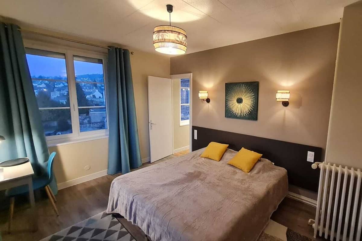 Habitación de hotel con una cama grande, un escritorio y vista a la ciudad por la ventana.