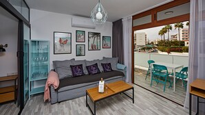 A modern living room with a sofa, coffee table, and teal chairs. There are framed pictures on the wall and a glass cabinet with wine glasses.
