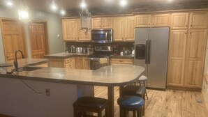A kitchen with wooden cabinets, a stainless steel refrigerator, a microwave, and a large island with stools.