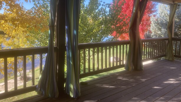 A covered outdoor deck with a wooden railing and curtains.