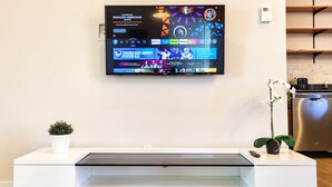 Una cocina moderna con una televisión integrada que muestra la interfaz de un servicio de streaming, un refrigerador de acero inoxidable y una encimera blanca minimalista.