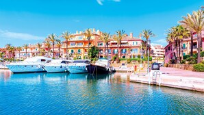 Een jachthaven met verschillende jachten die aanmeren, omringd door kleurrijke gebouwen en palmbomen.