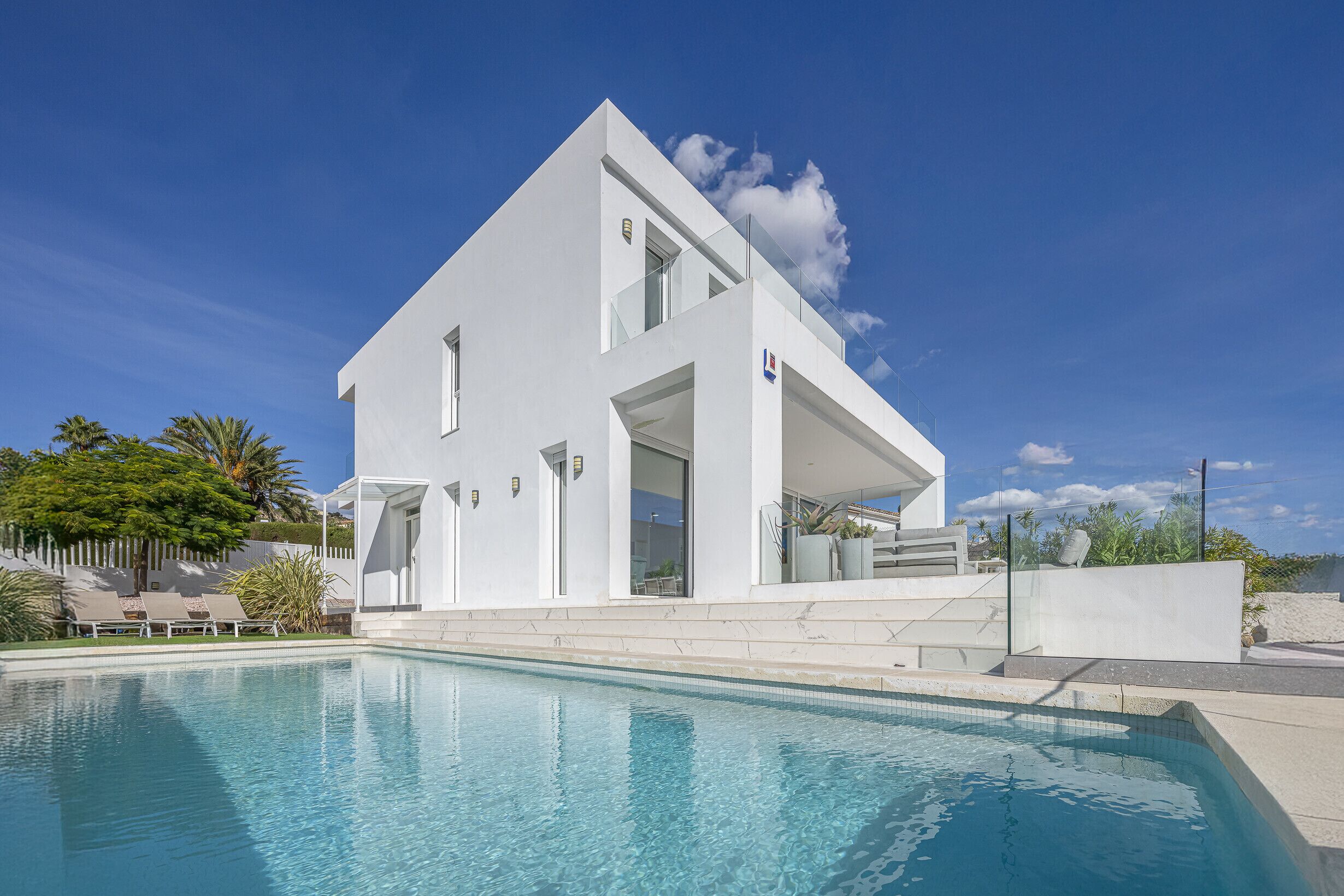 A modern white house with a swimming pool, large windows, and a balcony.