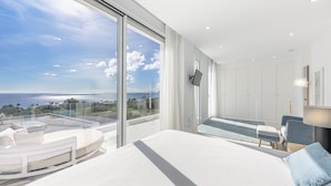 Een moderne slaapkamer met een groot bed, een zithoek met uitzicht op de oceaan en een balkon met een glazen reling.