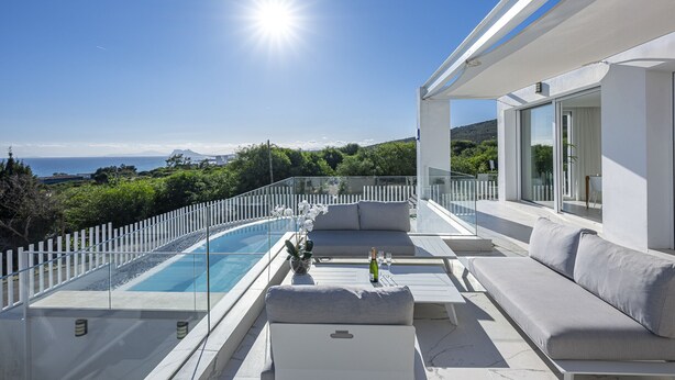 A modern outdoor terrace with a glass infinity pool, a white sofa, and a dining table. - Villa EDEN 2399 private pool & sea view (San Roque)