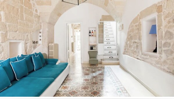 A living room with a stone wall, a blue sofa, a patterned rug, and a white cabinet with drawers.