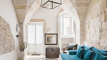 A living room with a stone wall, a blue sofa, a wooden chest, and a framed picture on the wall.