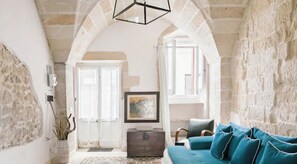 A living room with a stone wall, a blue sofa, a wooden chest, and a framed picture on the wall.