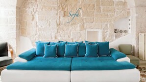 A room with a stone wall, a sofa with blue cushions, and a white armchair.
