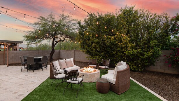 Eine Terrasse im Freien mit Feuerstelle, Sitzgelegenheiten und Lichterketten vor einem Sonnenuntergangshimmel.