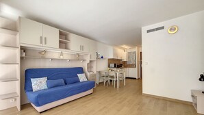 A compact living space with a blue sofa, a kitchenette, and a dining area.